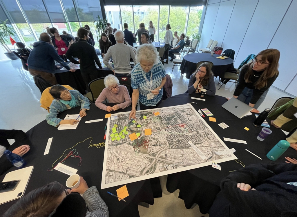Diverse group of community members assembled around a large map, engaged in a brainstorming activity with post-it notes.